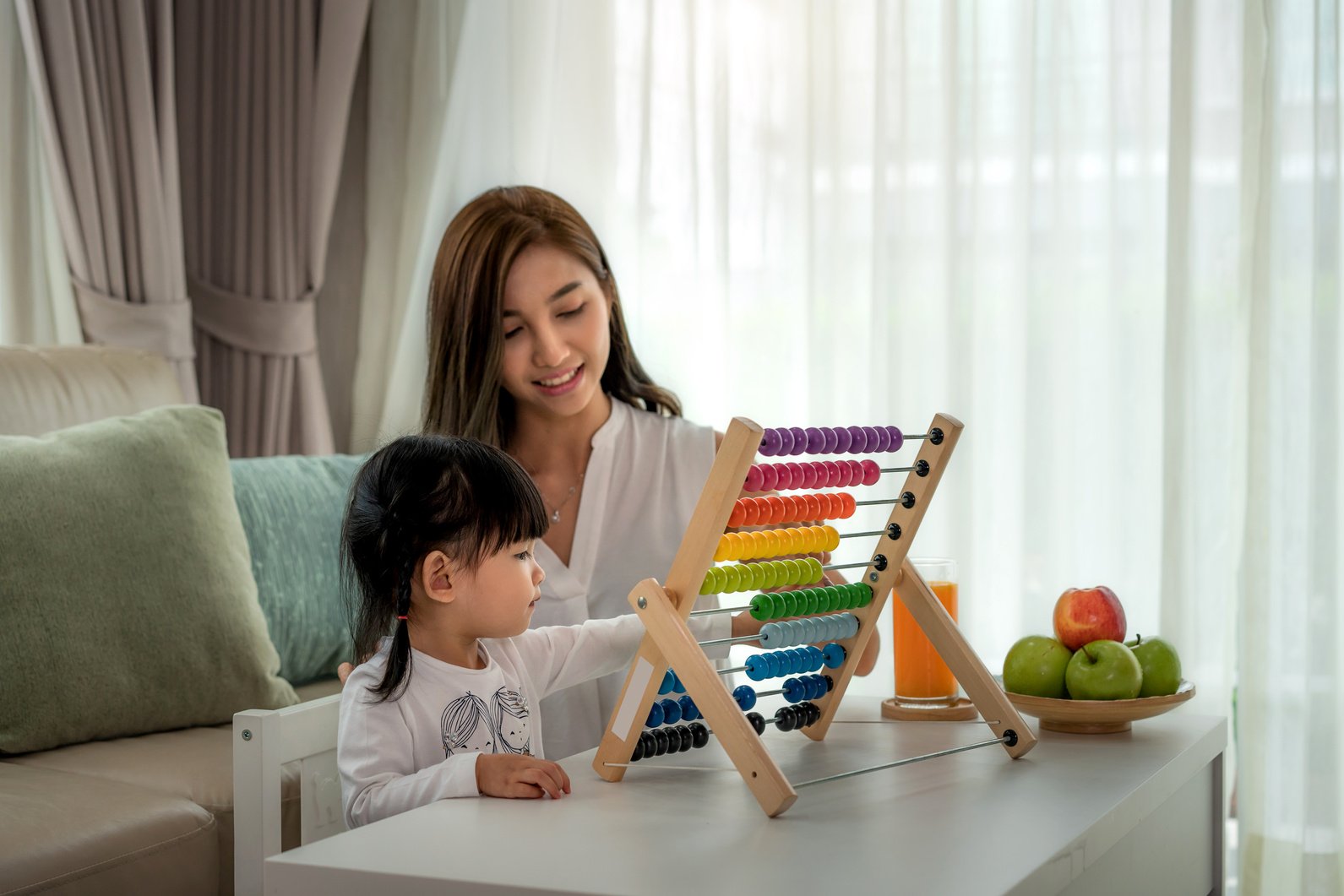 Happy Asian young mother and daughter playing with abacus, early education at home.